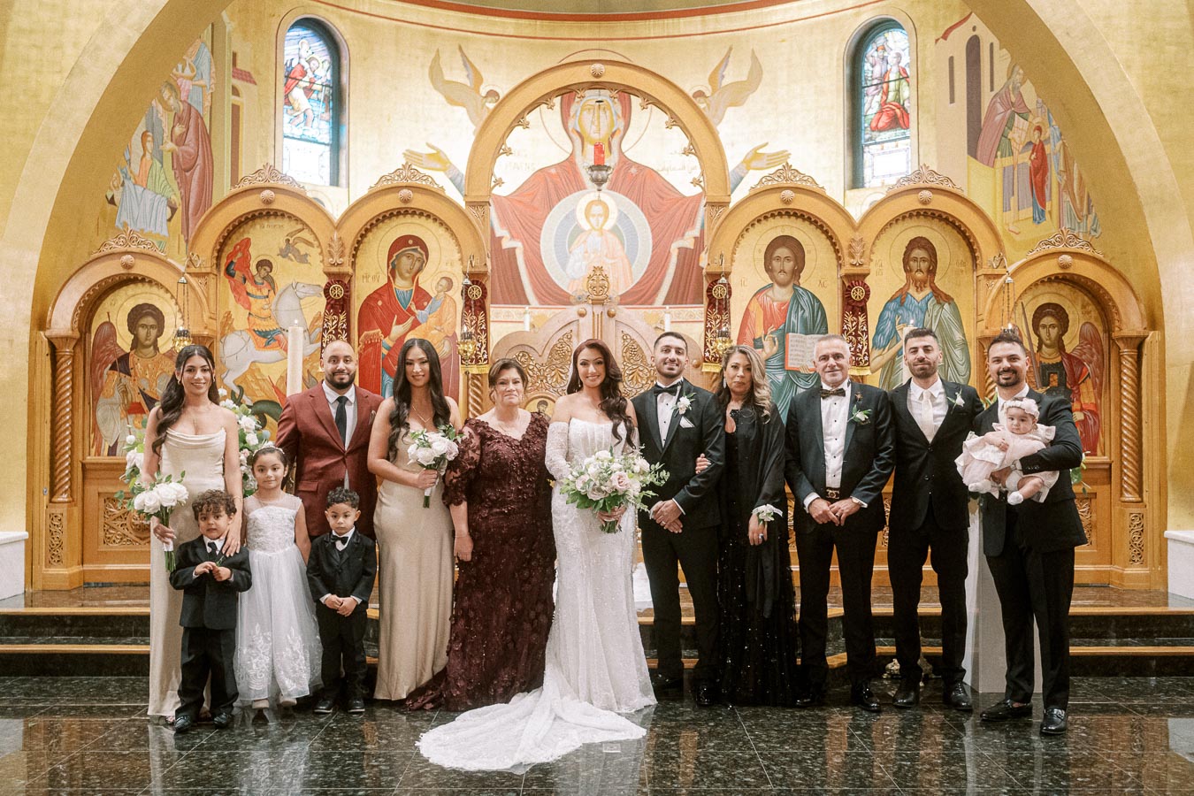 A large family standing together in formal attire inside a beautifully decorated church with ornate religious icons,