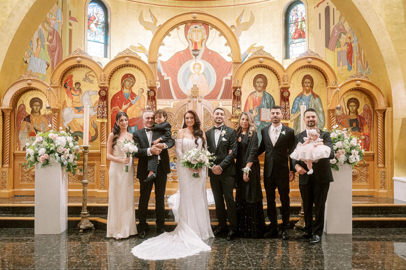 A joyful wedding ceremony in an ornate church setting featuring the bride and groom surrounded by family members. The
