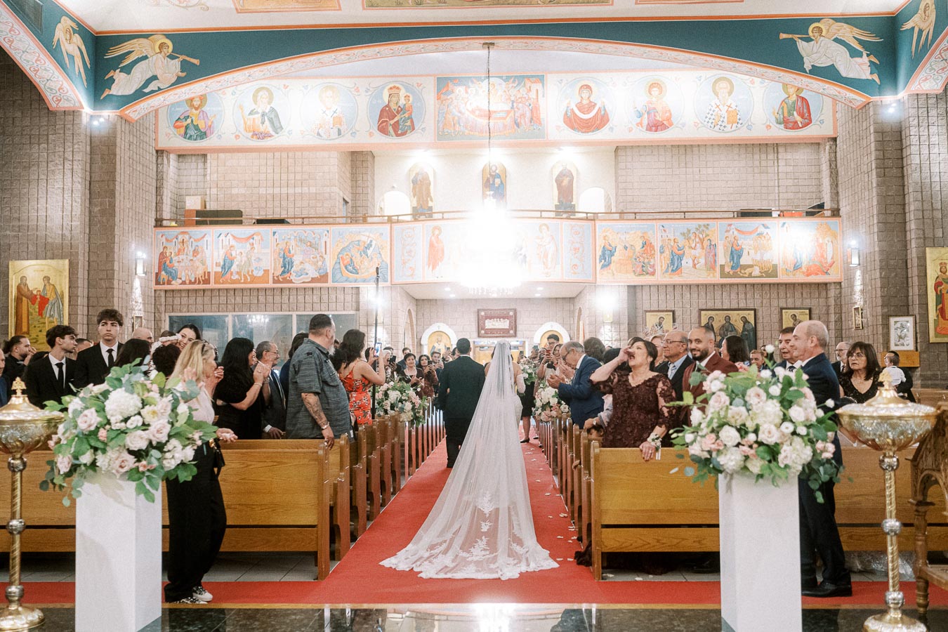 Bride and groom walking down the aisle in a beautifully decorated church adorned with frescoes and floral arrangements,