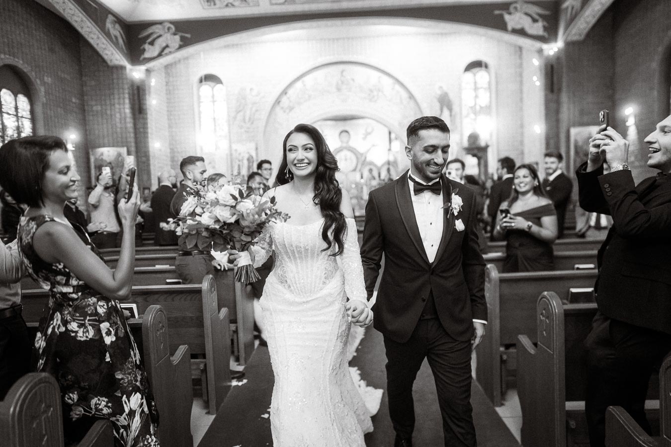 A joyful bride and groom walking down the aisle holding hands in a beautifully decorated church, surrounded by smiling