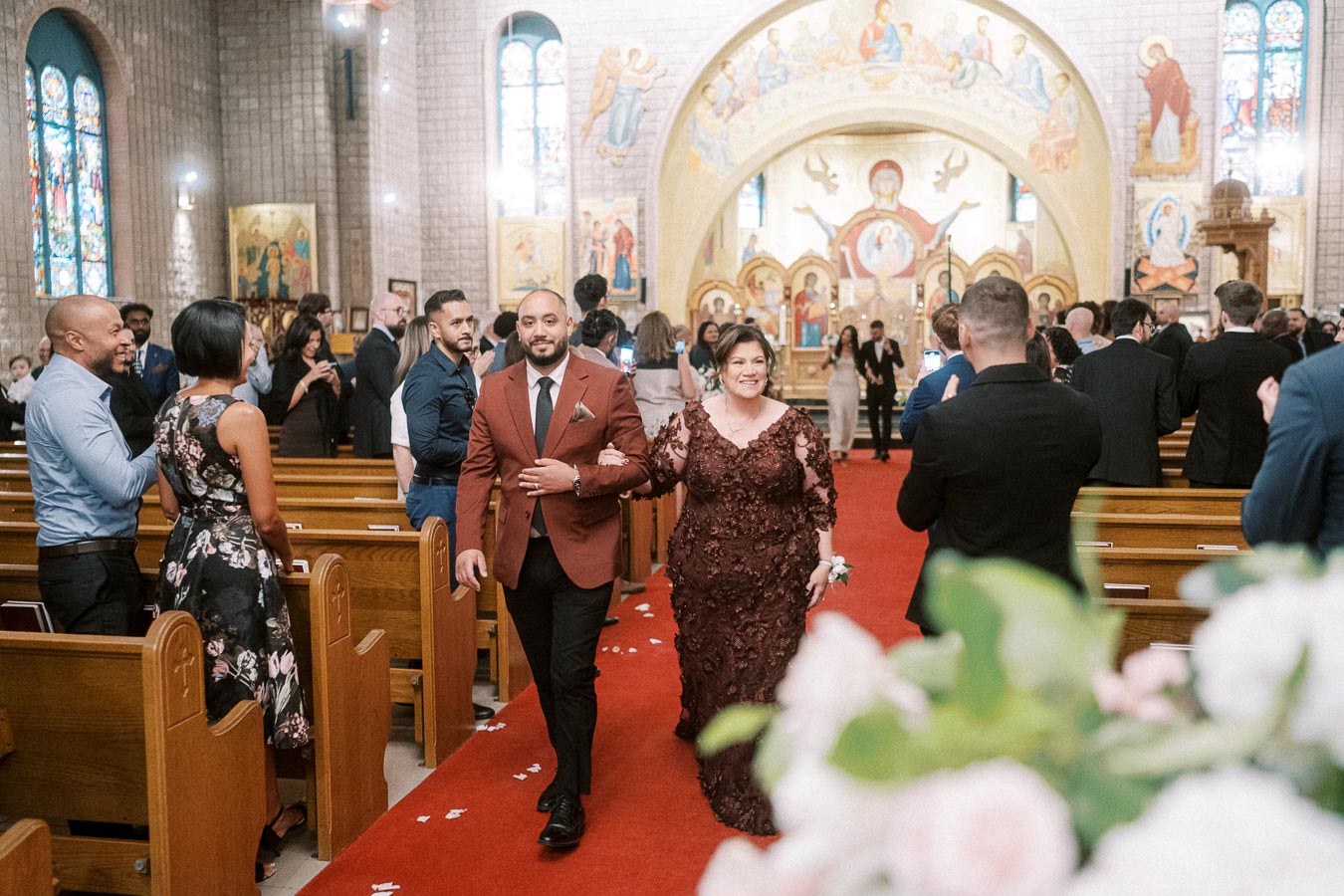 A couple elegantly walks down the aisle of a beautifully decorated church during a wedding ceremony, surrounded by guests