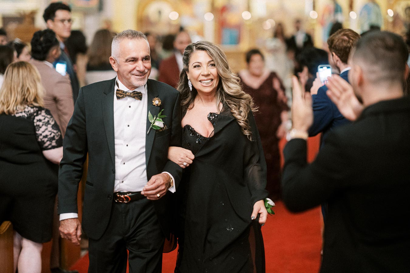 A smiling couple walking down the red carpet at a formal event, surrounded by a cheering crowd.