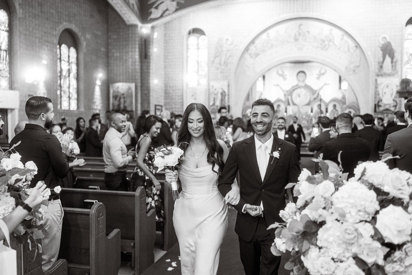 A joyful bride and groom exit a beautifully decorated church aisle after their wedding ceremony, surrounded by friends and