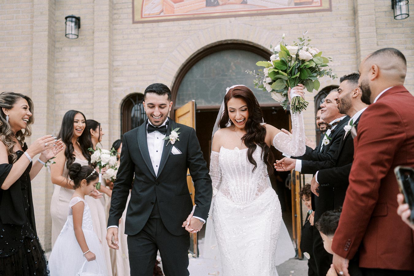 A joyful bride and groom holding hands as they walk out of a church after their wedding ceremony, surrounded by friends and