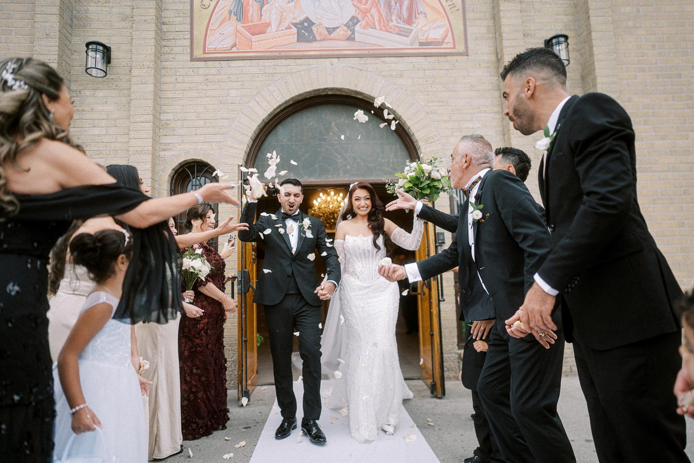 Bride and groom exiting a church as guests throw rose petals, celebrating their wedding day.