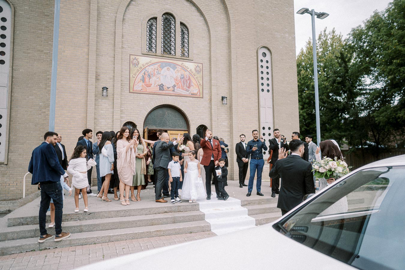 A group of well-dressed people gathered outside a church, celebrating a wedding ceremony with smiles and cameras, as the