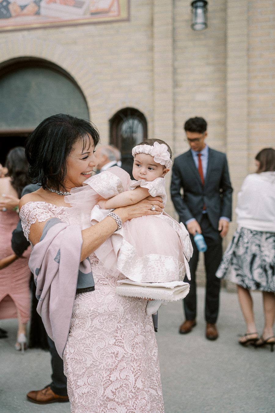 Grandmother joyfully holding her granddaughter in matching pink dresses at an outdoor family gathering.