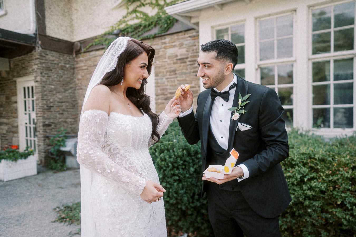 A bride in an elegant white wedding dress and veil shares a playful moment with a groom in a black tuxedo as they enjoy
