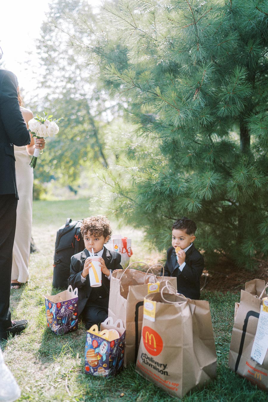 Young children in suits enjoying fast food from McDonald's at an outdoor gathering, surrounded by trees and paper bags