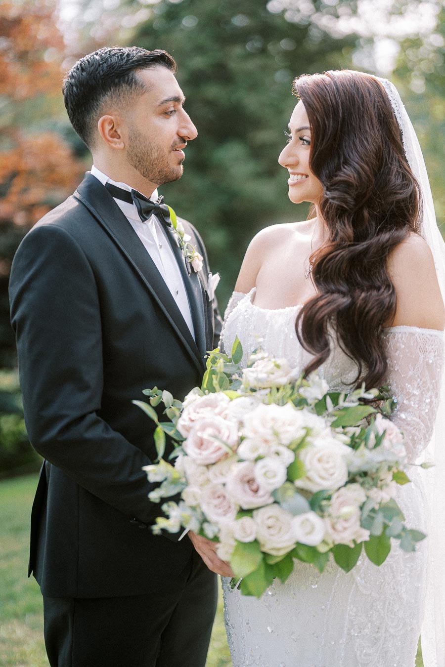 A bride and groom gaze lovingly at each other during their outdoor wedding, with the bride holding a lush bouquet of white