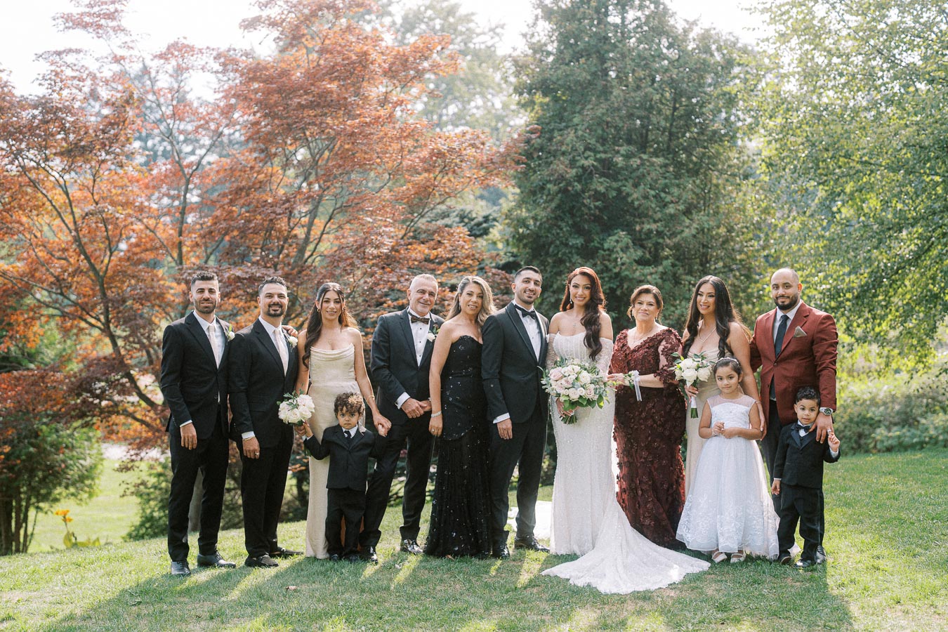 A diverse wedding party posing outdoors in elegant attire, with bridesmaids in stylish dresses and groomsmen in suits,
