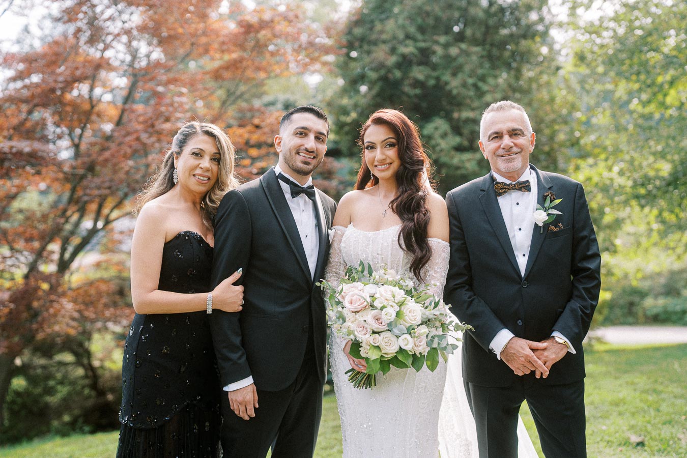 Elegant garden wedding portrait featuring a bride in a white gown holding a bouquet of roses, groom in a tuxedo, and