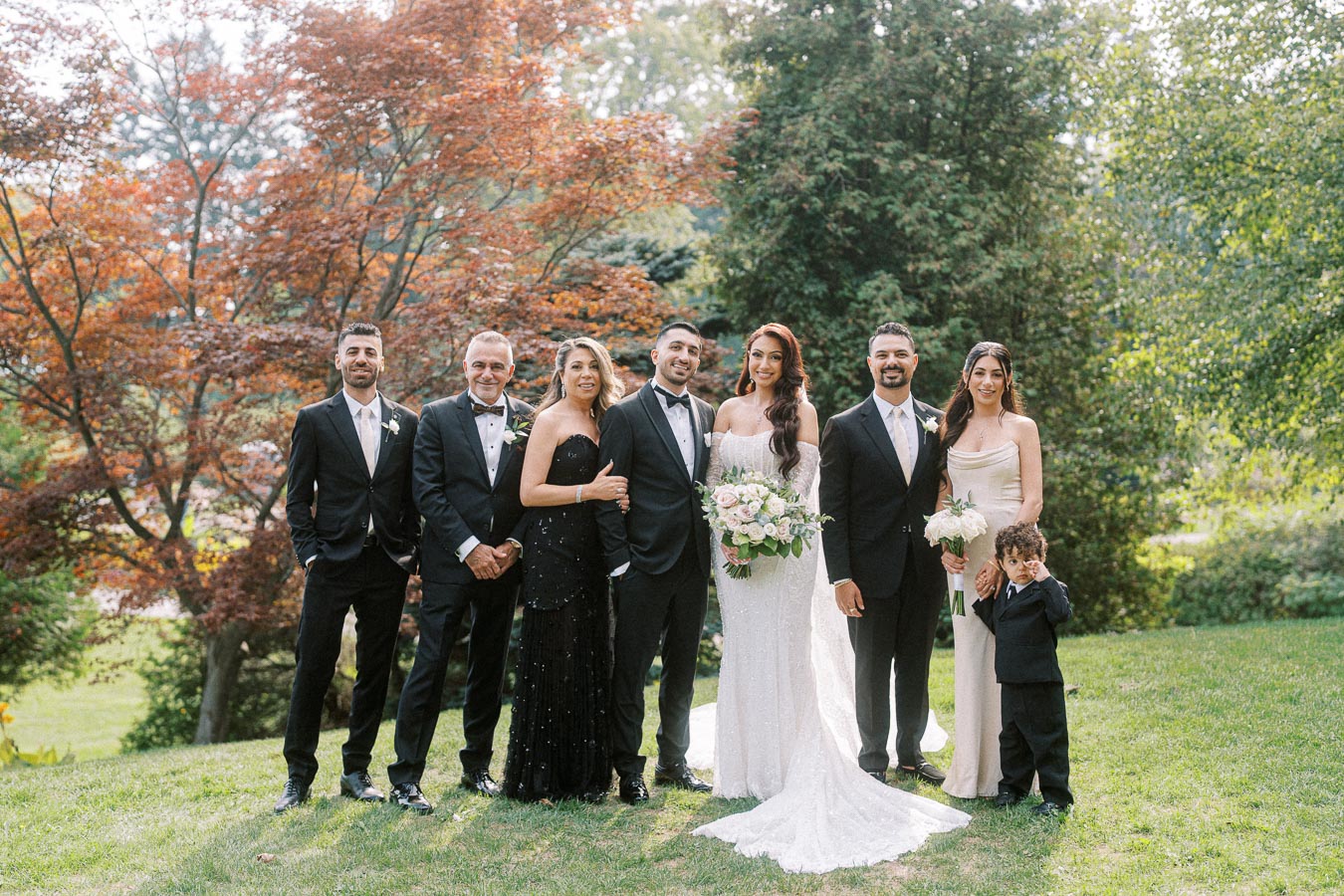 Wedding party posed in a lush garden setting, featuring elegantly dressed guests, including the bride in a white gown