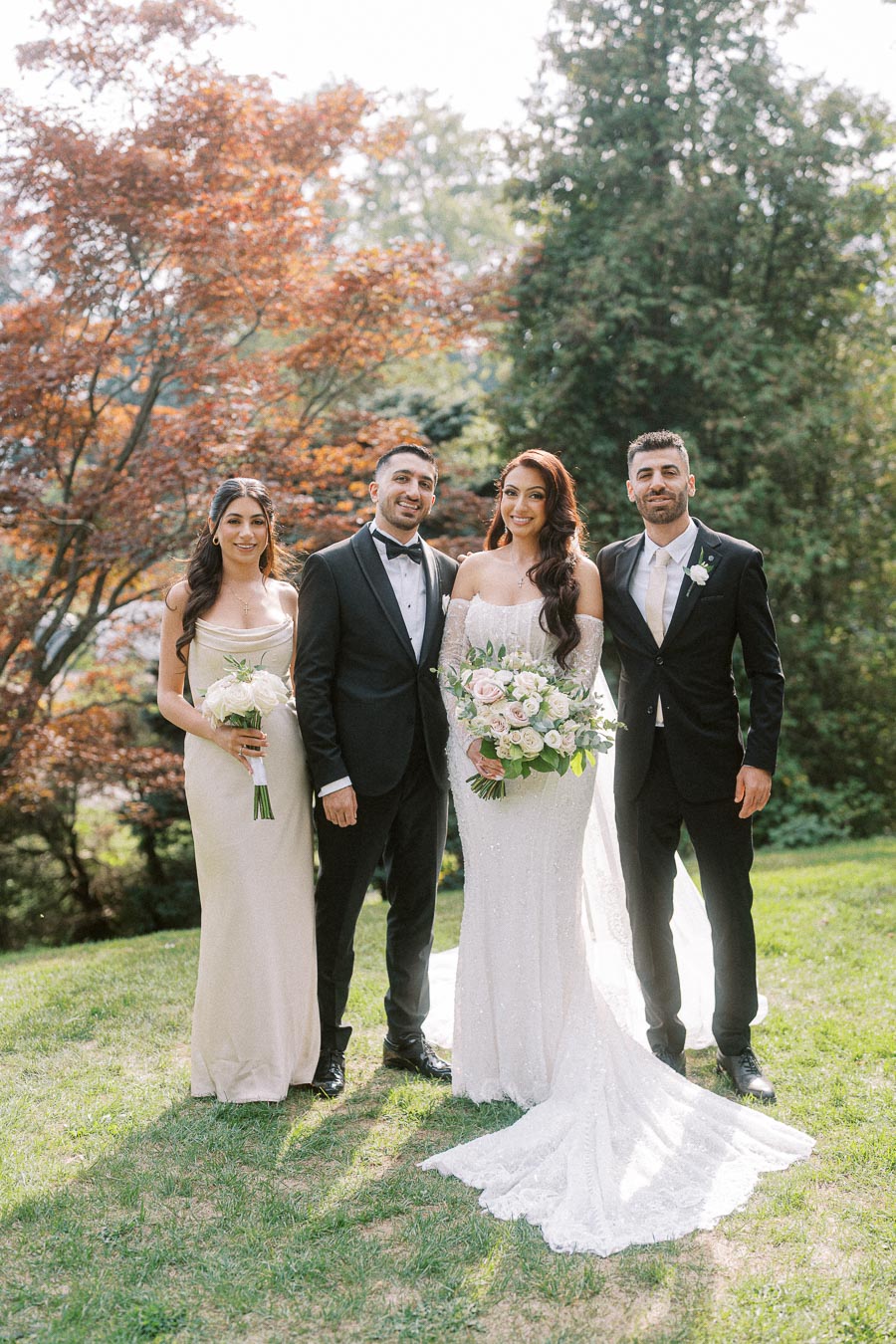 Wedding party posing outdoors with the bride in a white gown, holding a bouquet, standing next to three elegantly dressed