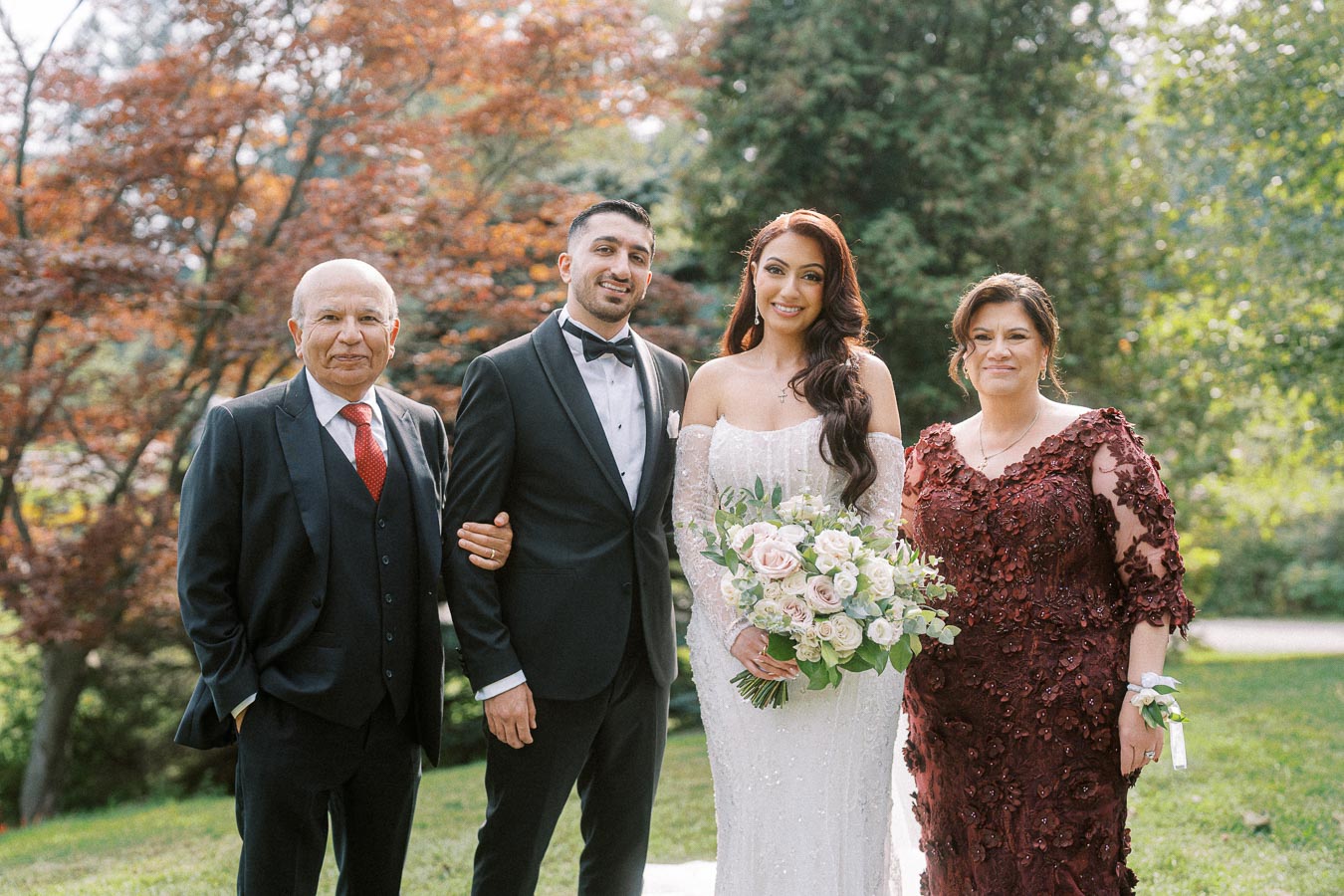 A bride and groom posing with family in a lush garden setting, showcasing elegant wedding attire; bride holding a bouquet of