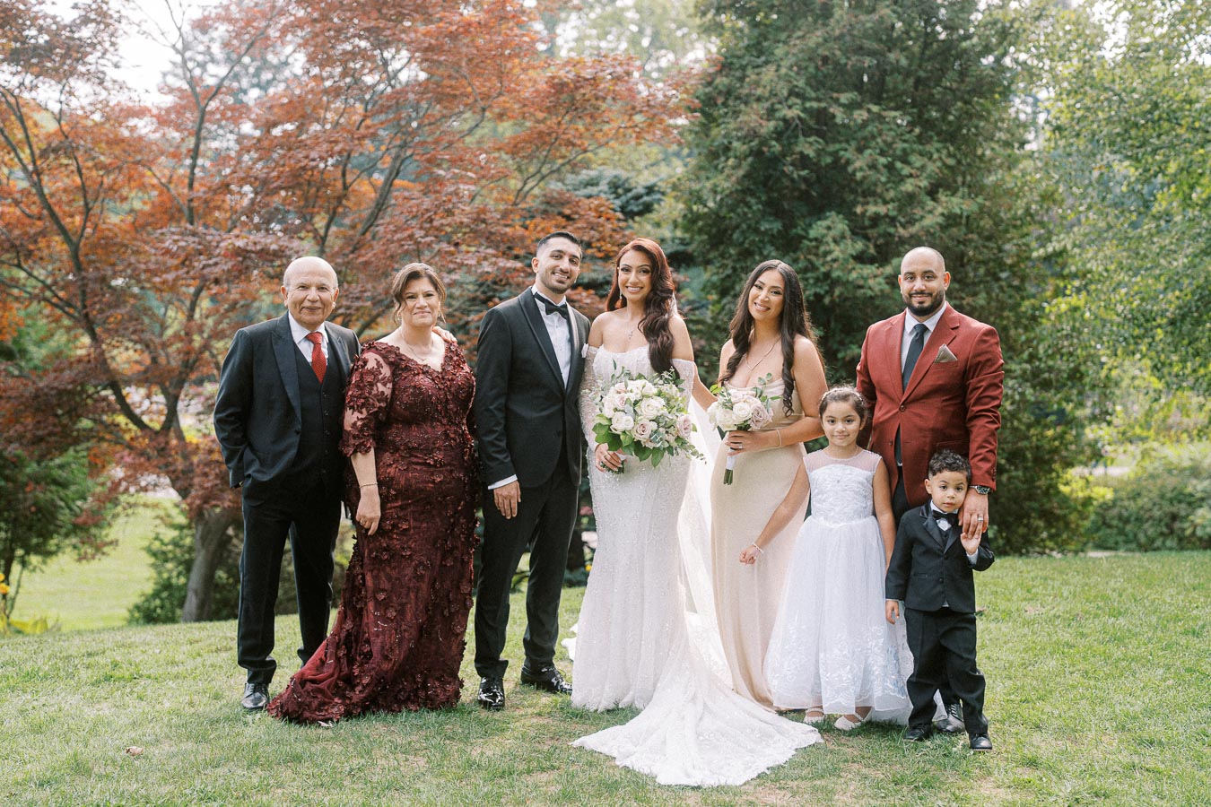 A family group at an outdoor wedding, featuring the bride in a white gown holding a bouquet, surrounded by family members in