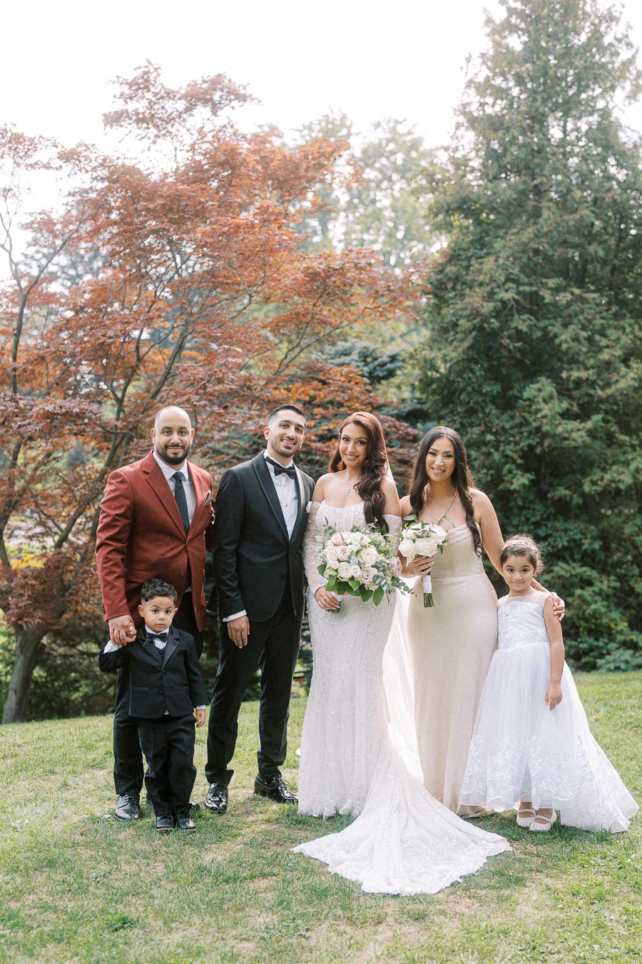 A happy family poses together at an outdoor wedding, featuring the bride in a white gown holding a bouquet, surrounded by
