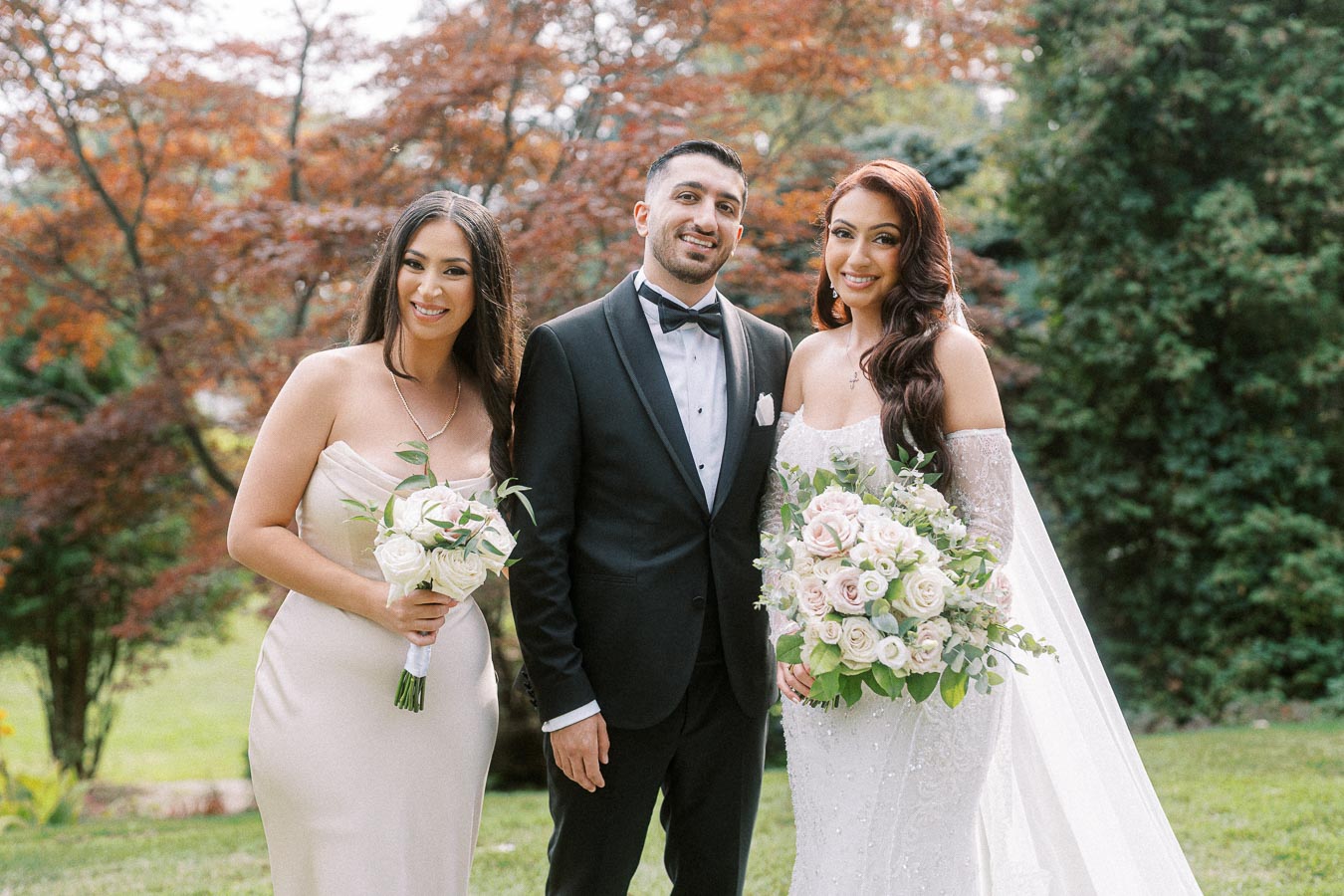 Wedding portrait of a bride in a white gown holding a bouquet of roses, standing beside the groom in a black tuxedo and a