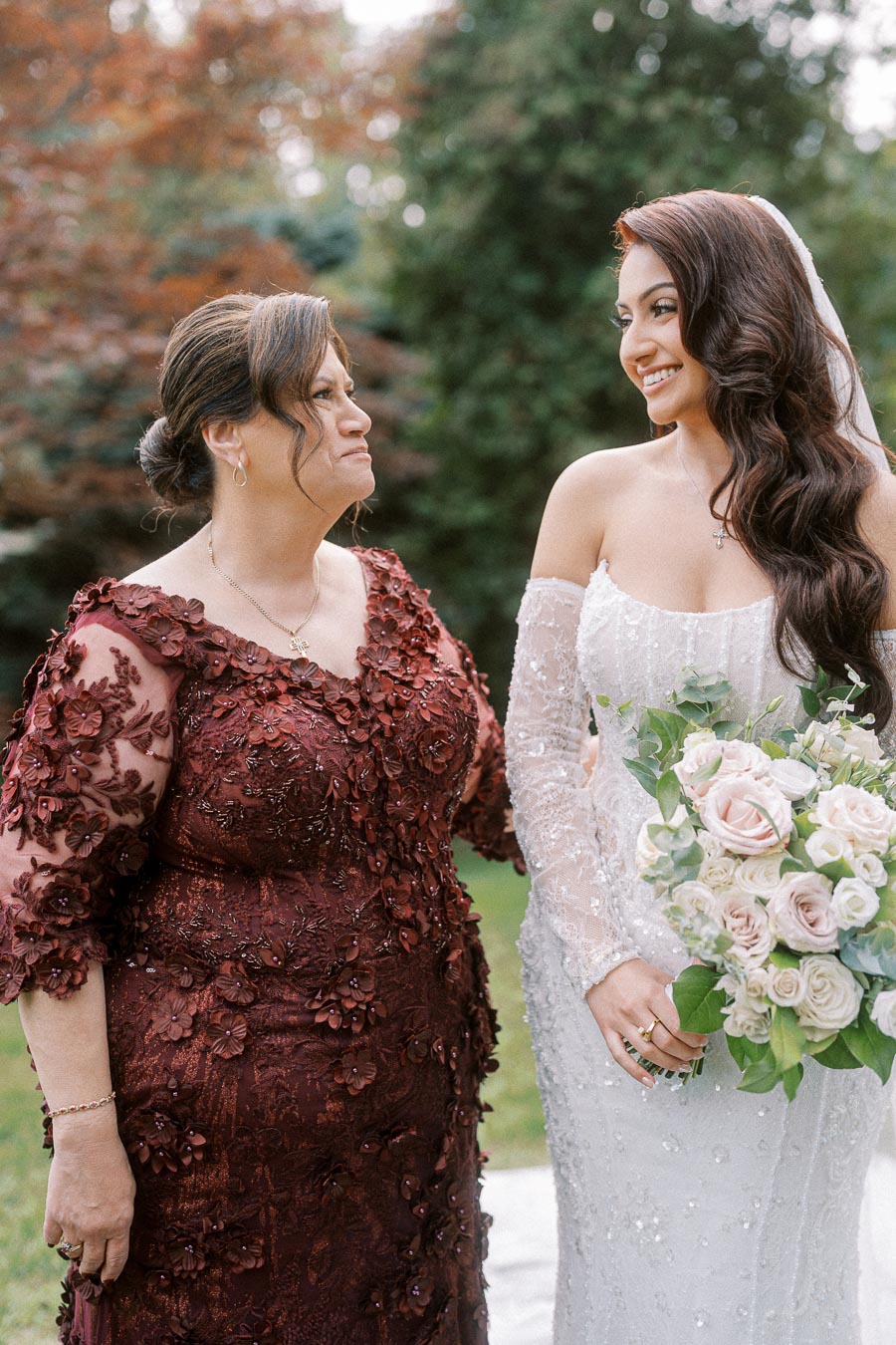 Bridal fashion captured outdoors: A bride in an elegant white wedding dress with lace detailing smiles at a woman in a