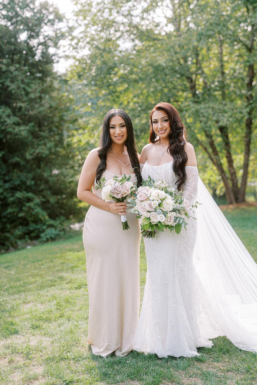 Bridal party photo featuring a bride in a white gown and veil with a bouquet of roses, standing next to a bridesmaid in a