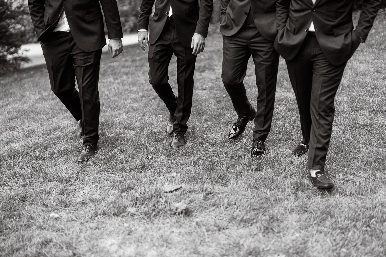 Black and white photo of four men in suits walking on grass, emphasizing formal attire and outdoor setting.