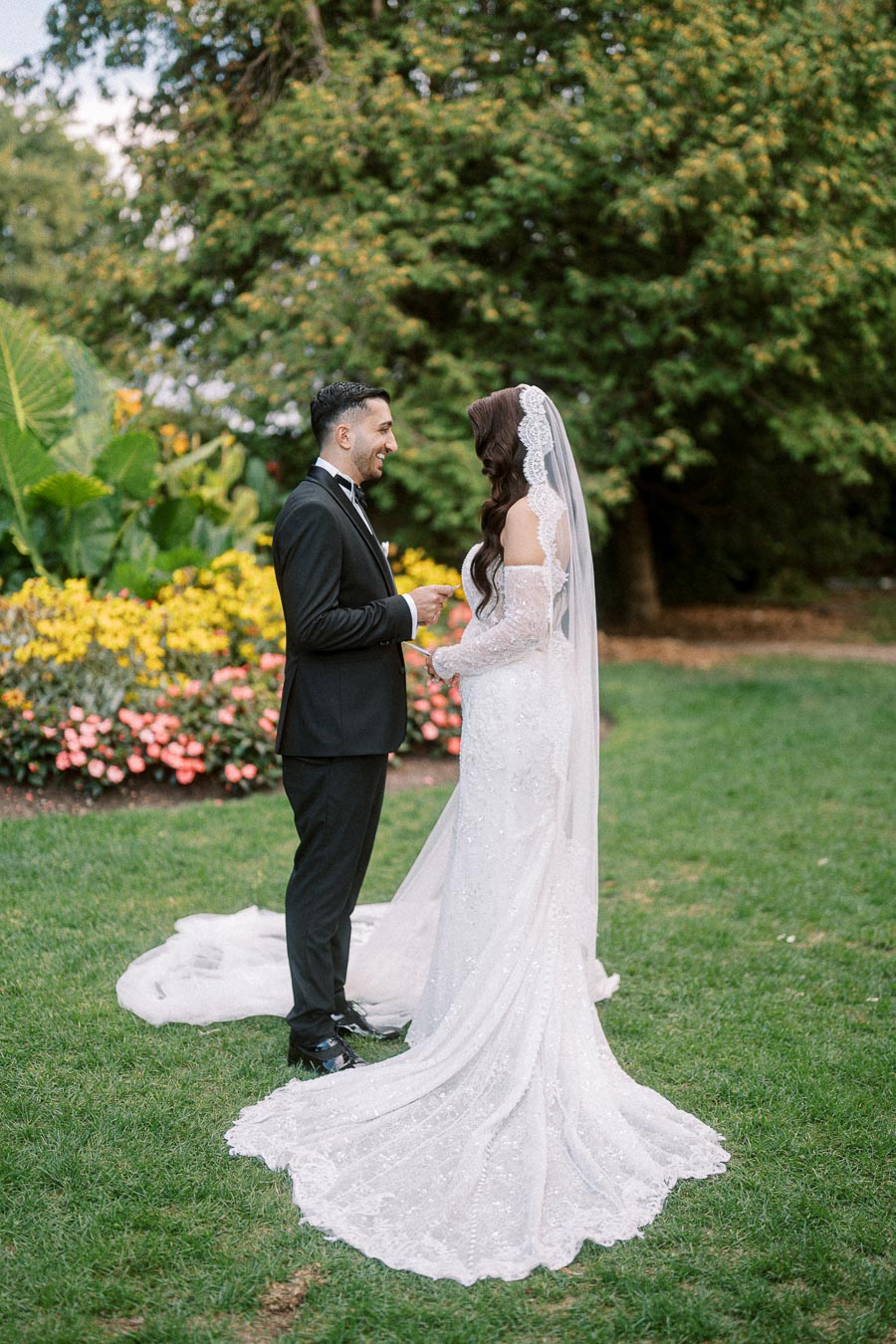 Bride and groom exchanging vows in a lush garden setting, with the bride in a lace wedding gown and veil, and the groom in a