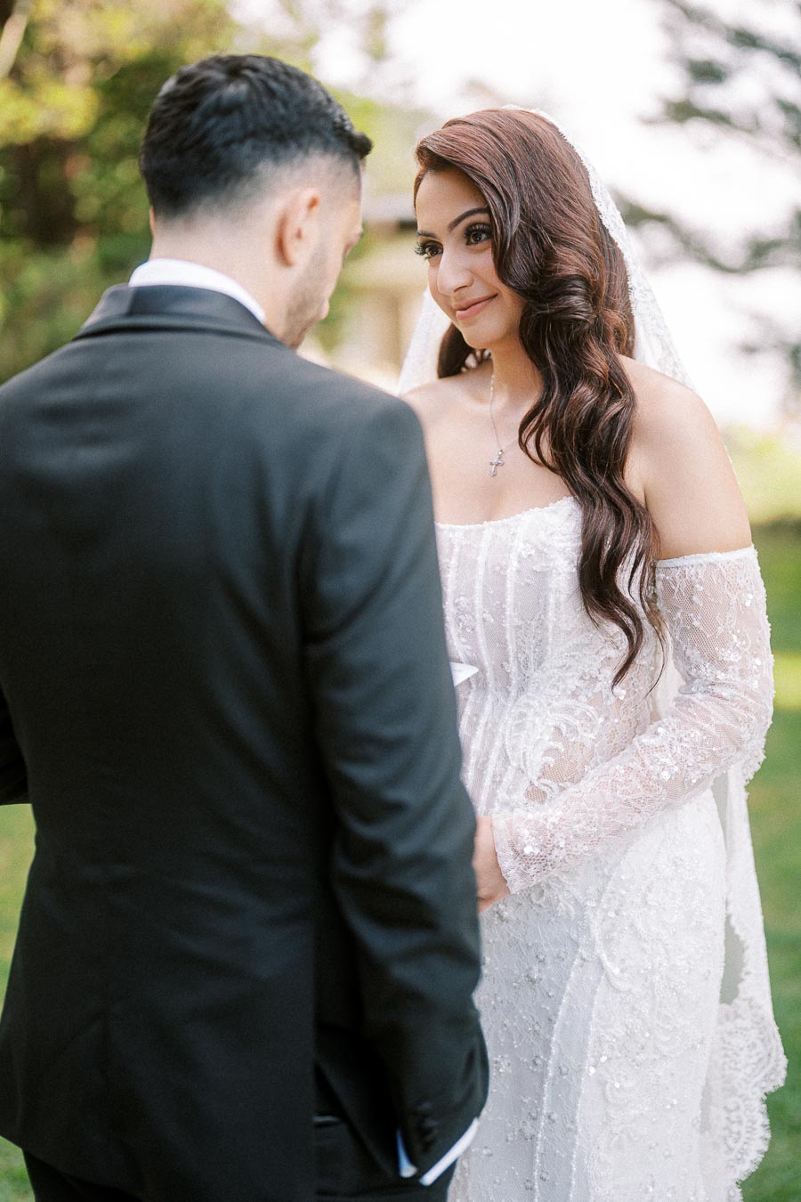 Bride and groom sharing a tender moment during outdoor wedding ceremony, with the bride in a lace bridal gown and the groom