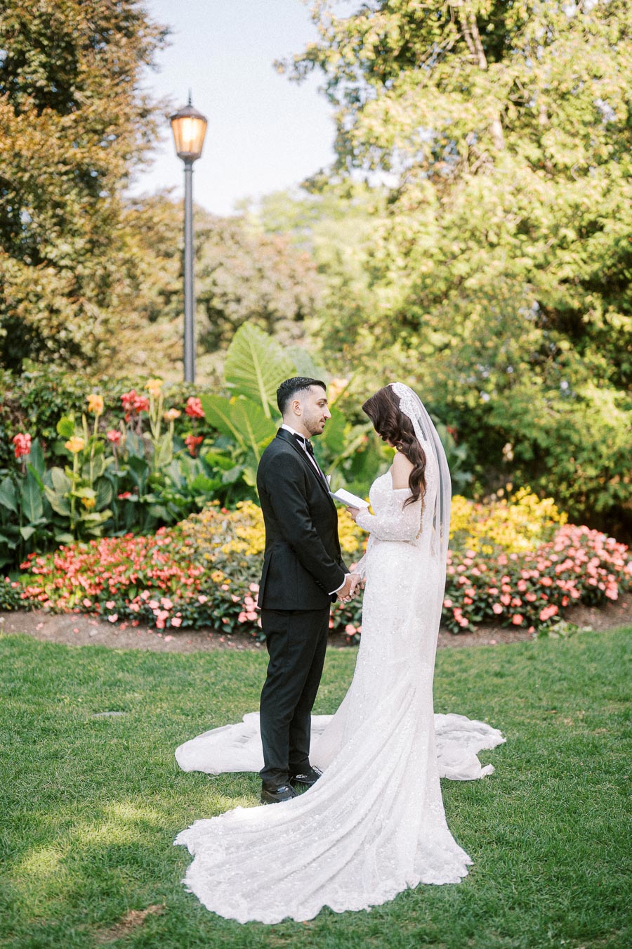 Bride and groom exchanging vows in a beautiful garden setting, surrounded by vibrant flowers and greenery, on a sunny day.