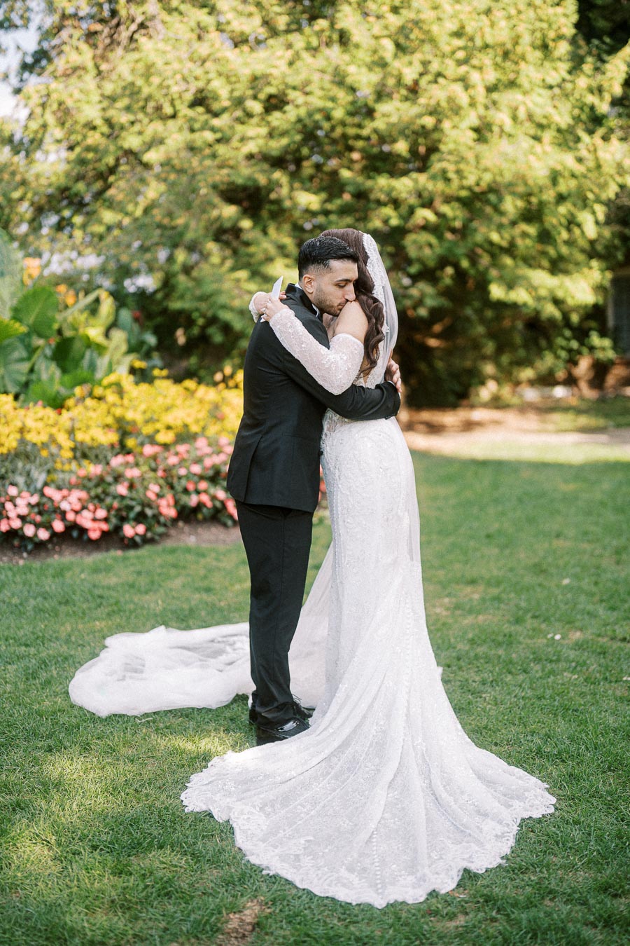 Bride and groom embracing in a lush garden setting, with colorful flowers and greenery in the background, creating a