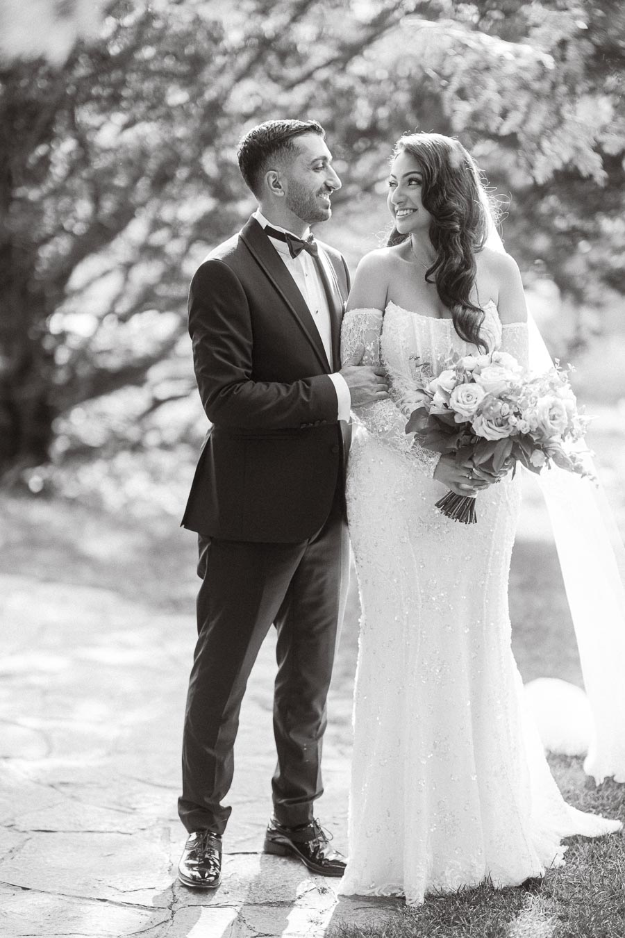 A bride and groom in elegant wedding attire share a joyful moment outdoors, with the bride holding a bouquet, depicted in a