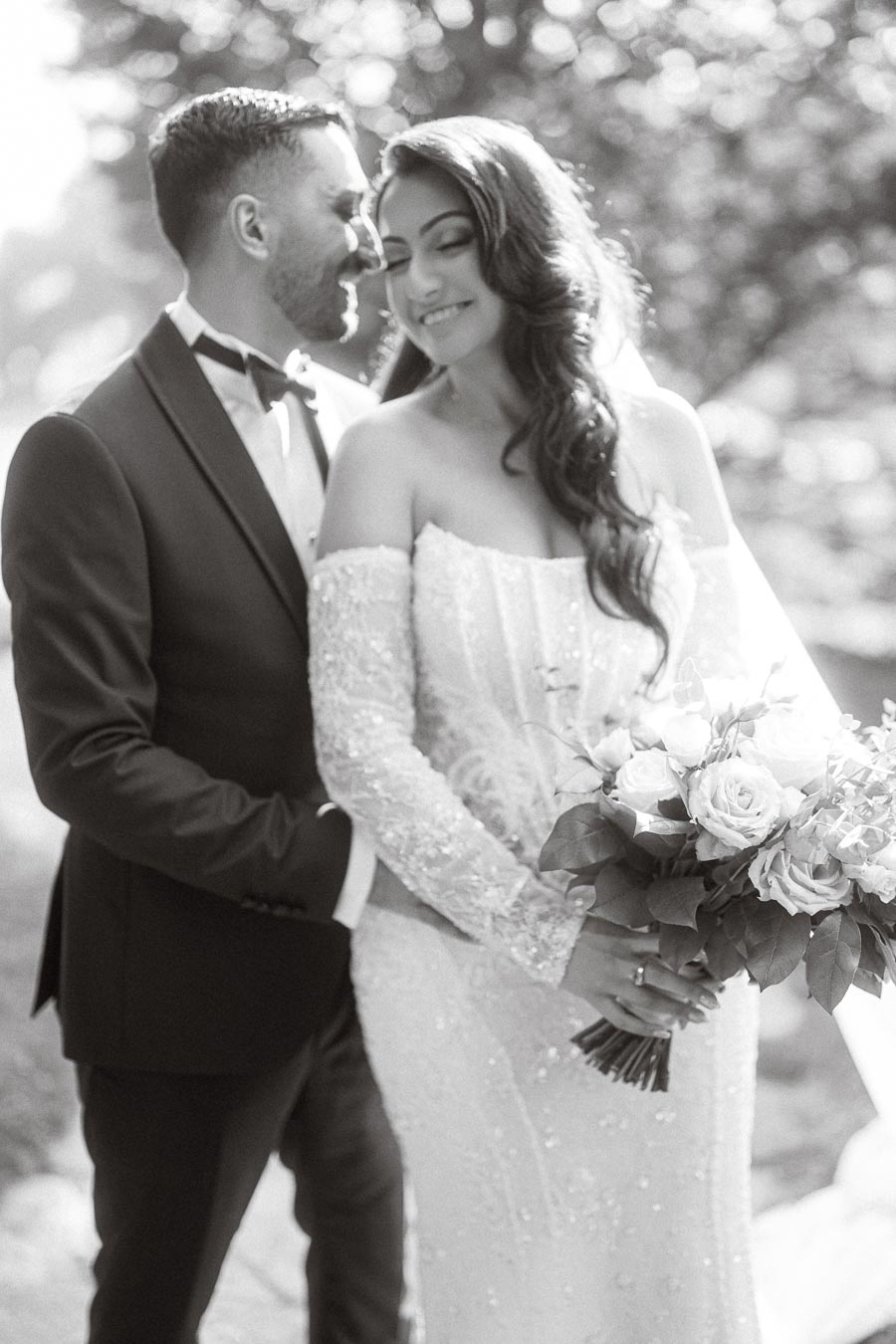 Black and white image of a couple in wedding attire, with the groom in a tuxedo and the bride in an off-the-shoulder gown