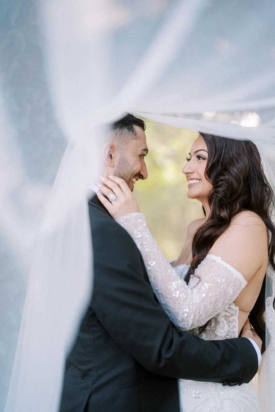 A couple embracing under a veil on their wedding day, smiling at each other with love and joy.