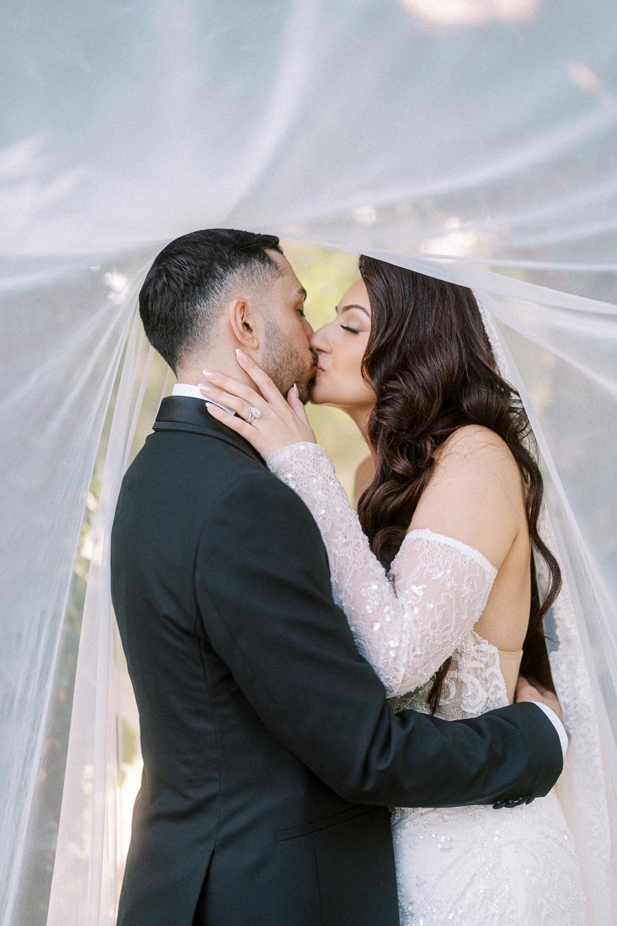 A bride and groom share a romantic kiss under a veil on their wedding day.