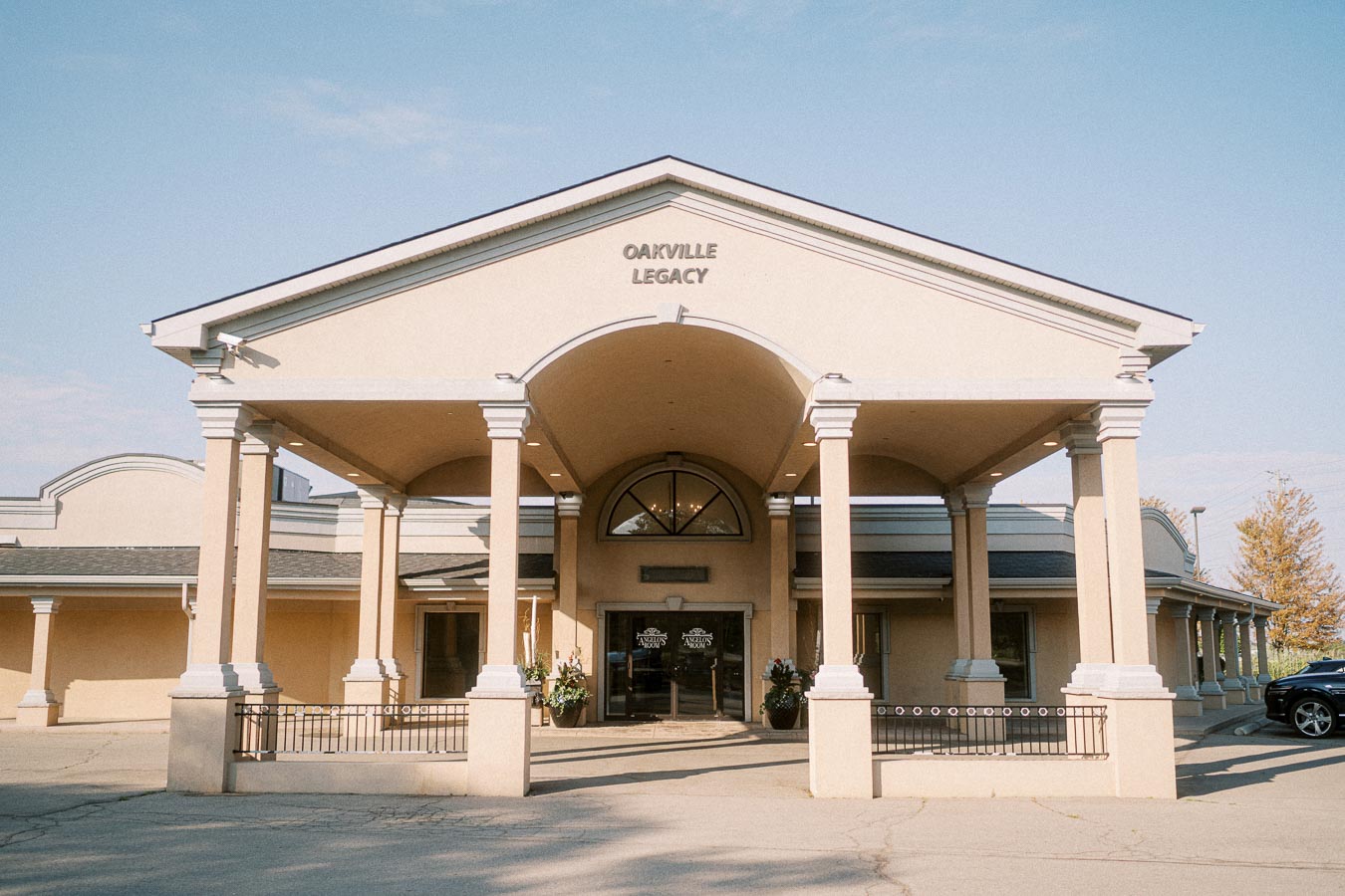 Grand entrance of Oakville Legacy building with elegant columns and decorative archway under a clear blue sky.