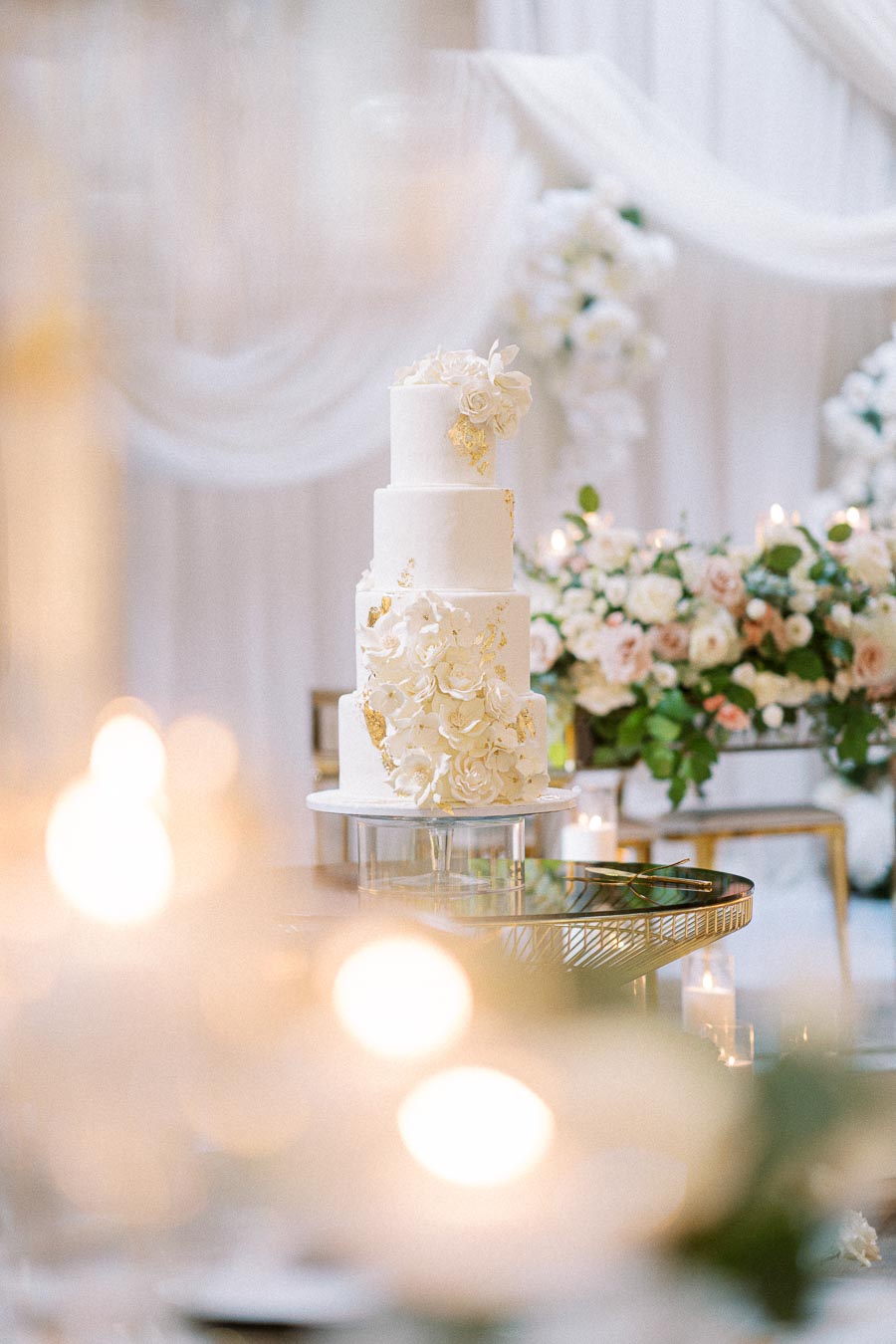 Elegant three-tier white wedding cake adorned with delicate floral decorations and gold accents, set against a beautifully