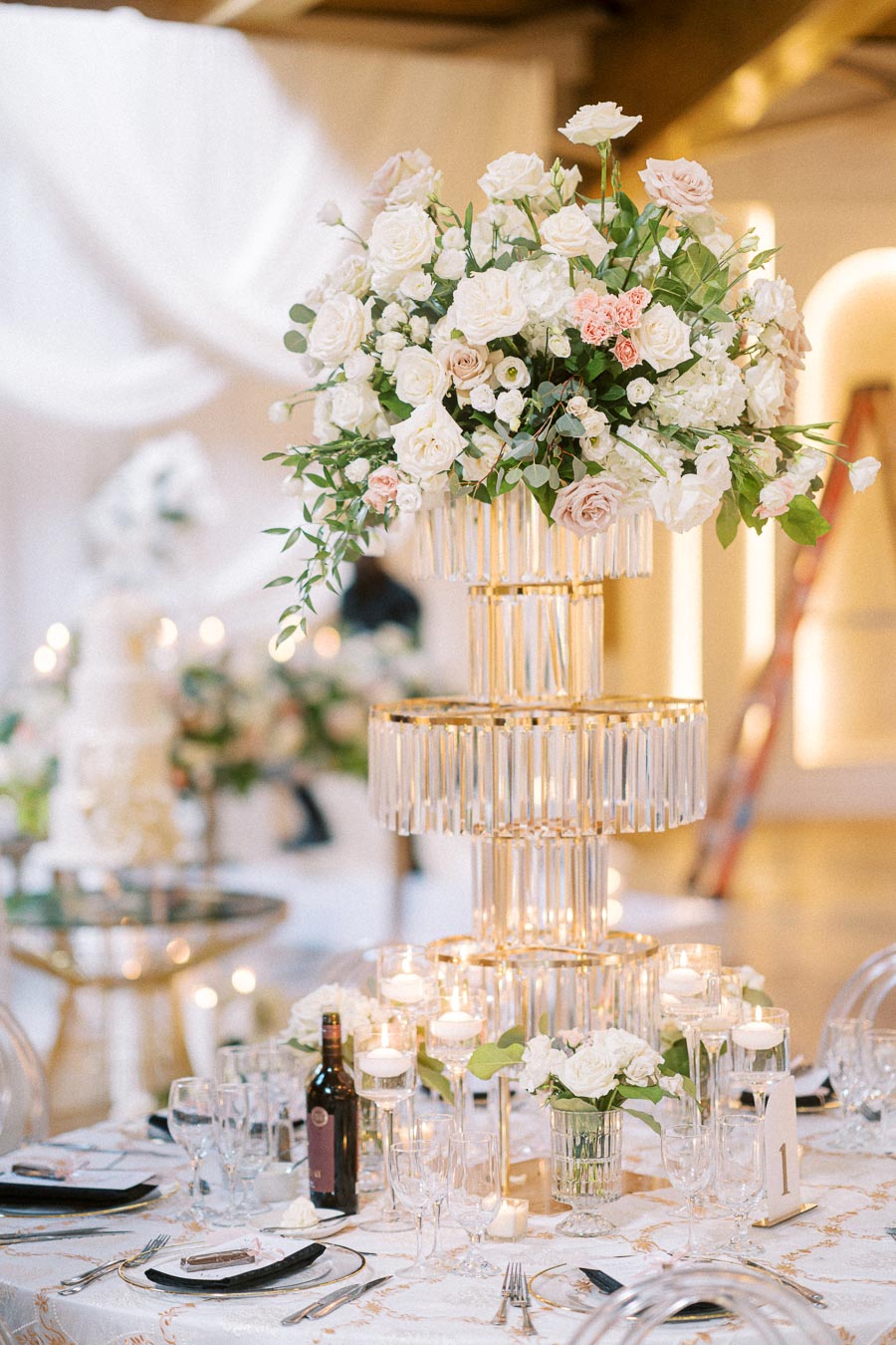 Elegant wedding reception table setting featuring a luxurious floral centerpiece with white and pink roses, crystal candle