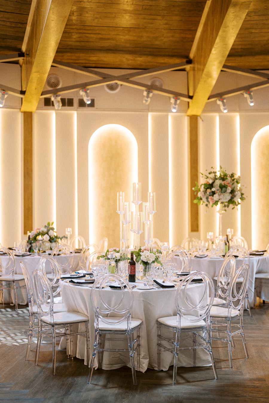 Elegant wedding reception setup with round tables covered in white tablecloths, adorned with floral centerpieces and tall