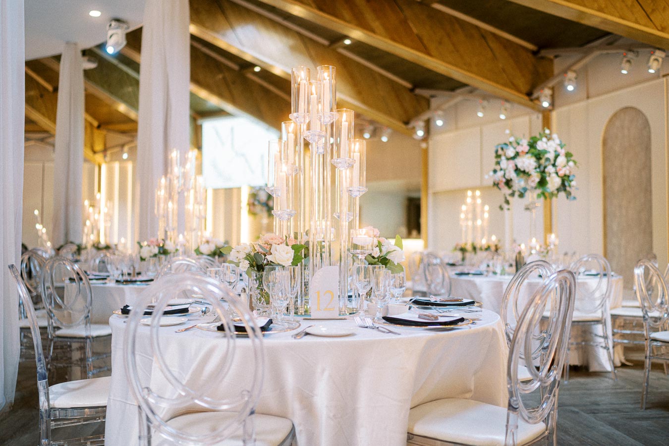 Elegant wedding reception venue with beautifully arranged round tables covered in white tablecloths. Tall glass candle