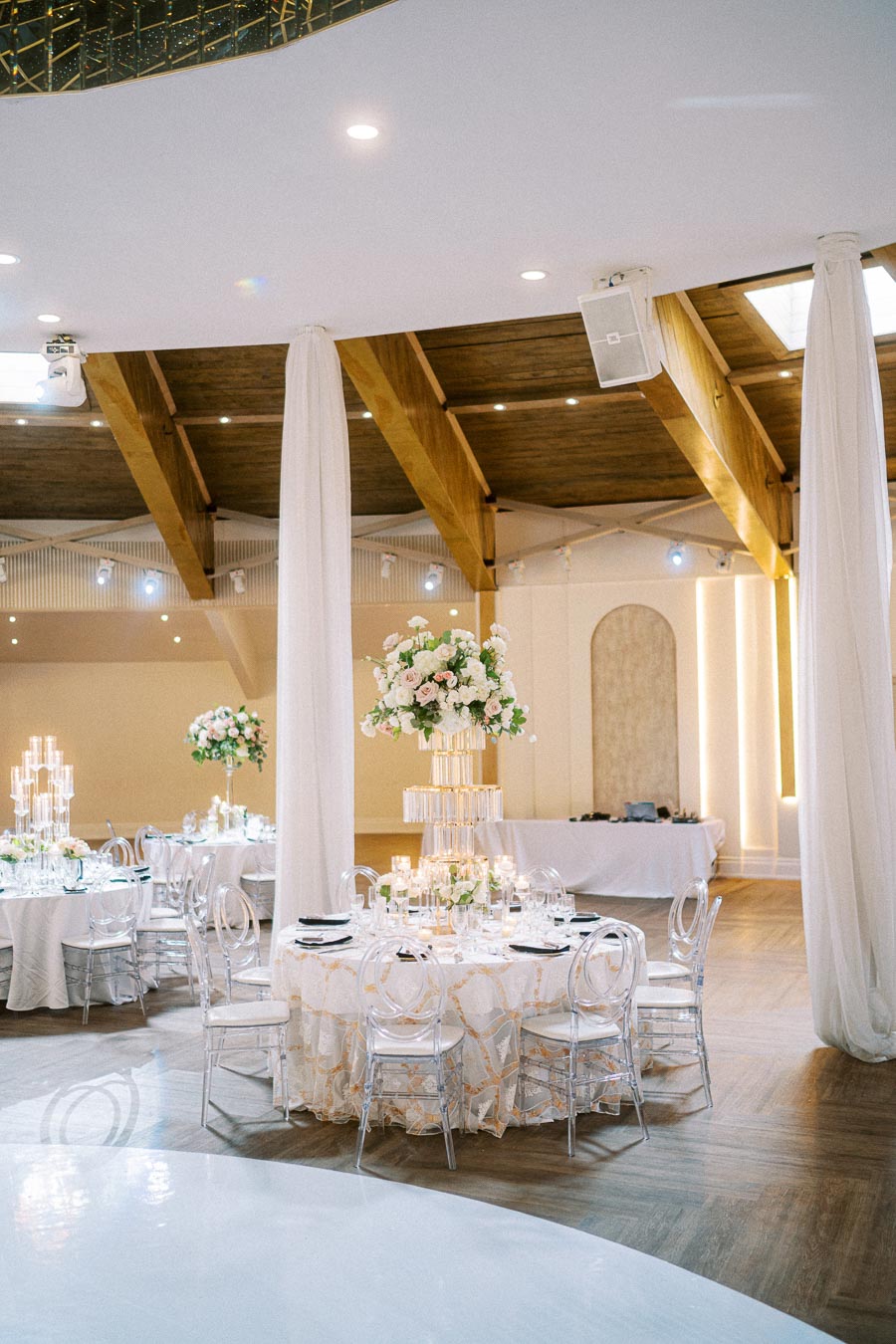 Elegant wedding reception venue with beautifully decorated tables, featuring tall floral centerpieces and clear chairs under