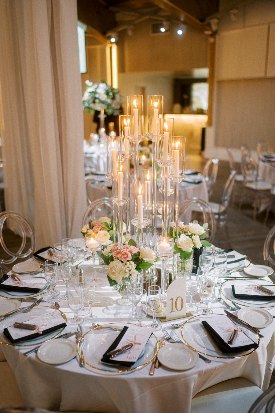 Elegant wedding reception table setting featuring tall candle centerpieces, floral arrangements with pink and white roses,