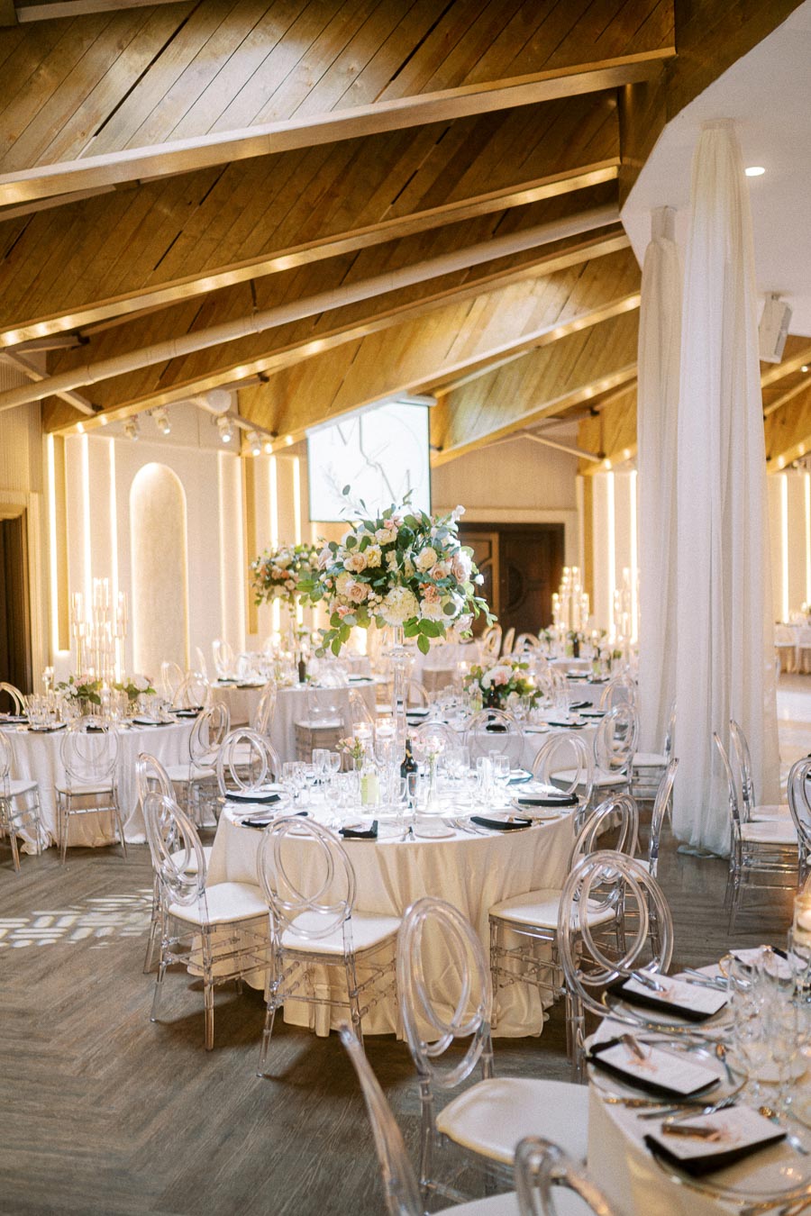 Elegant wedding reception venue with round tables adorned with white tablecloths, floral centerpieces, and transparent