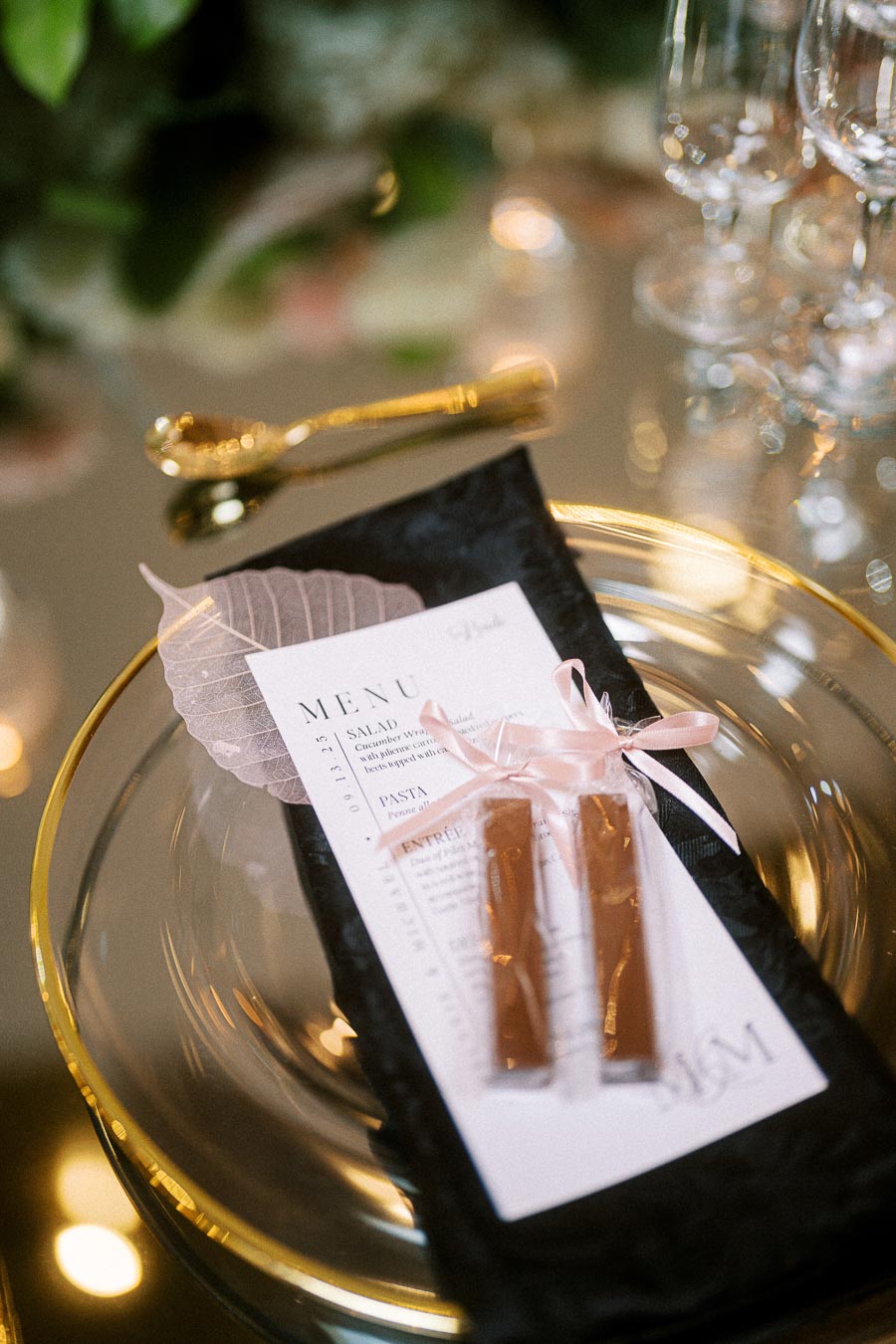 Elegant wedding table setting with a decorative menu card on a black napkin, adorned with a translucent leaf and tied with a
