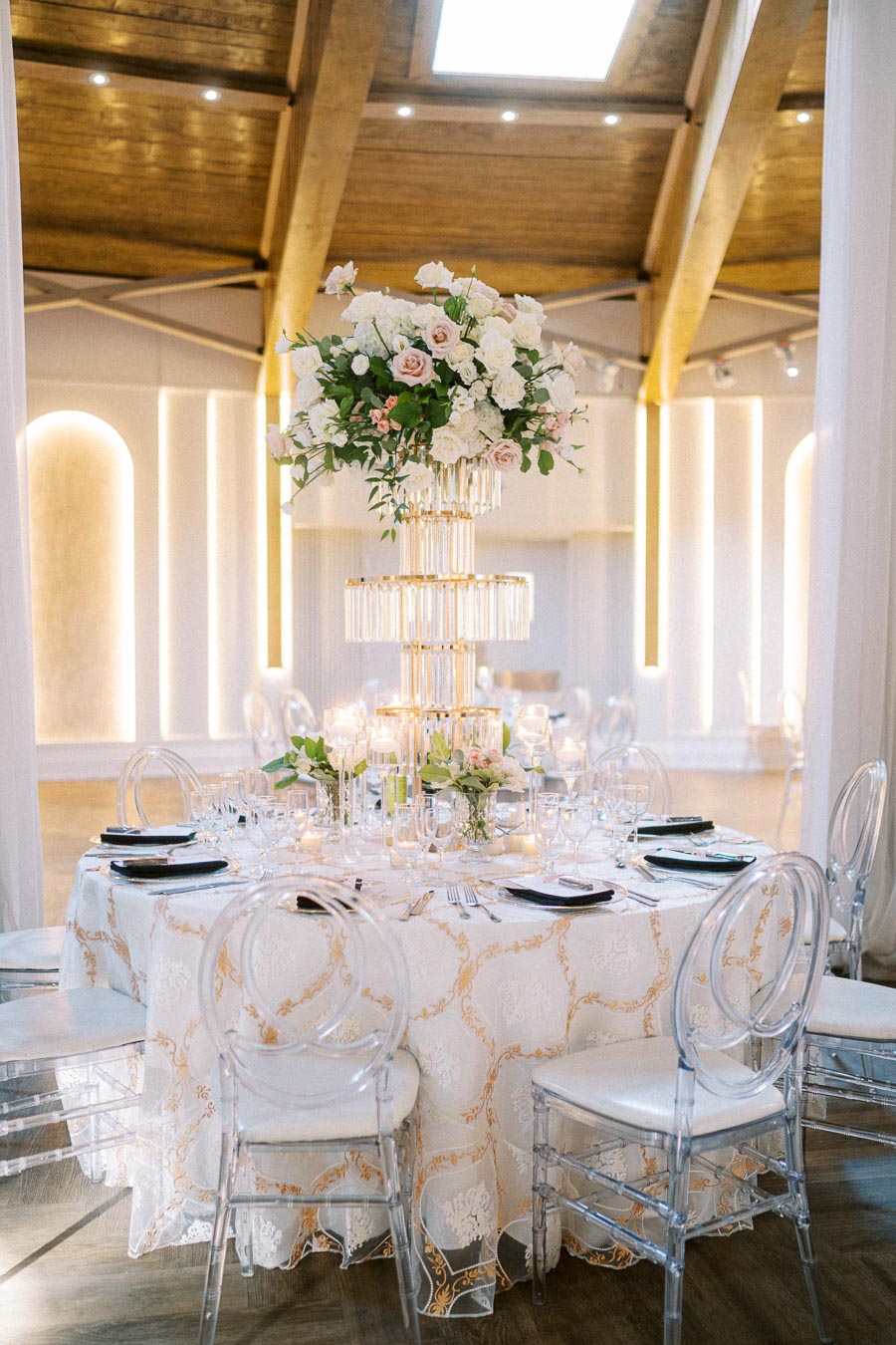 Elegant wedding reception table with a tall floral centerpiece, featuring white and blush roses, surrounded by glassware and