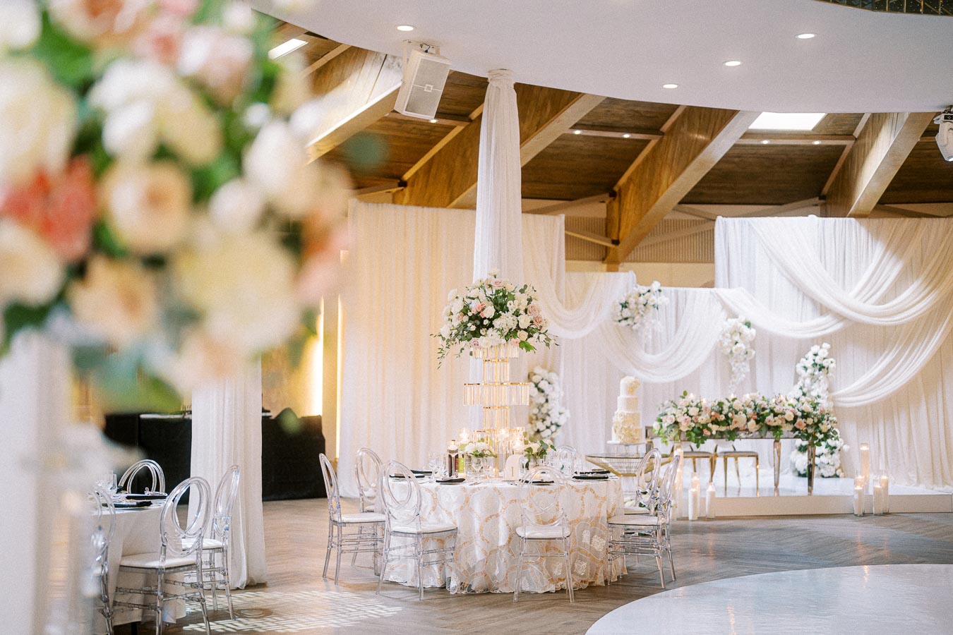 Elegant indoor wedding reception setup with a round table adorned with a lace tablecloth, floral centerpiece, and clear