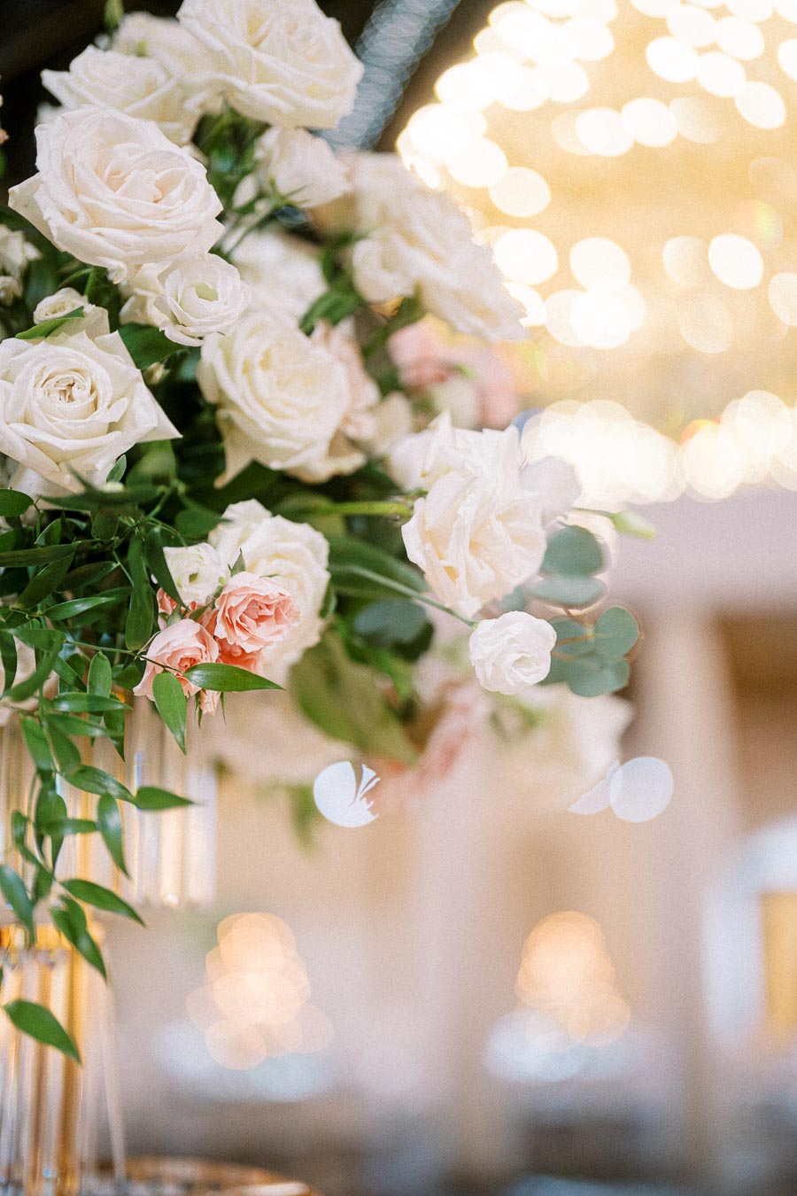 Elegant floral arrangement featuring white and light pink roses with green foliage, set against a softly blurred background