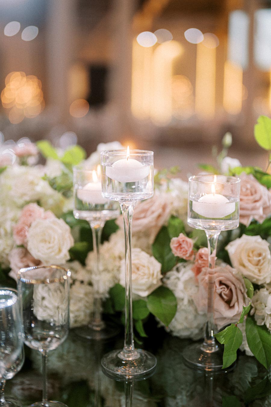 Elegant wedding table setting with floating candles in glass holders, surrounded by lush floral arrangements of white and