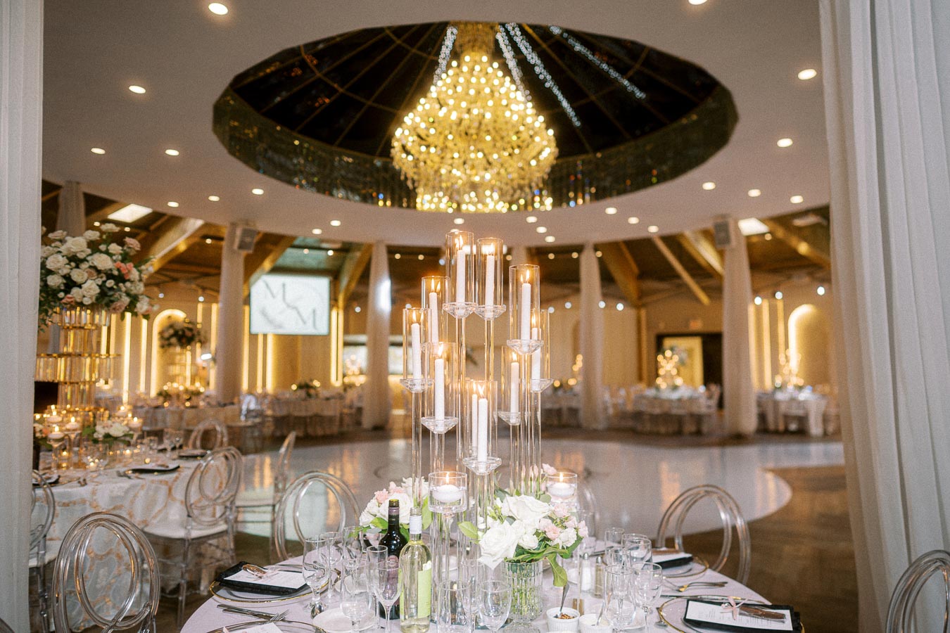 Elegant wedding venue with luxurious round tables set for reception, featuring tall glass candle holders and floral