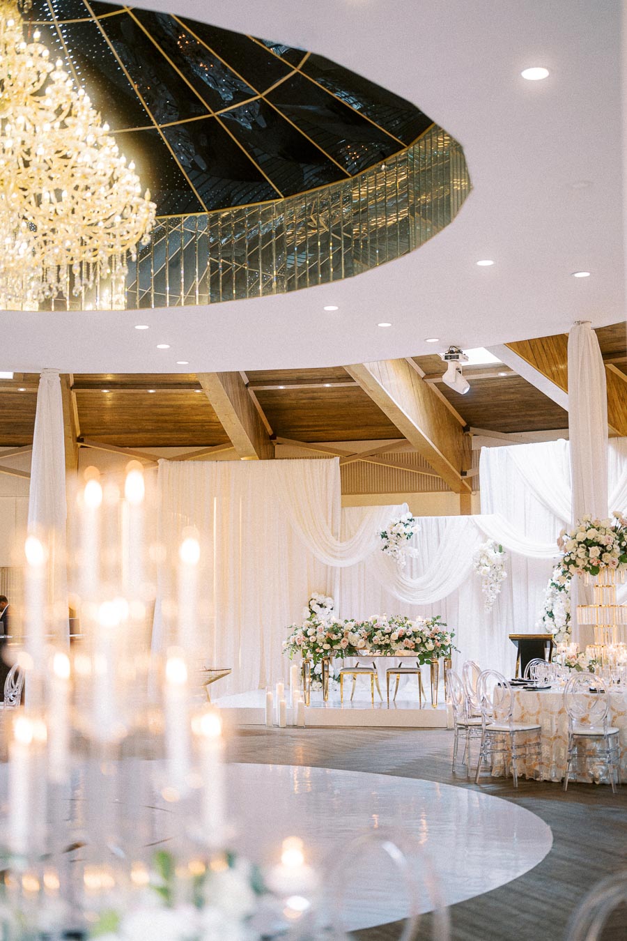 Luxurious wedding venue with elegant chandelier and floral decor, featuring white drapes and a beautifully set bridal table,