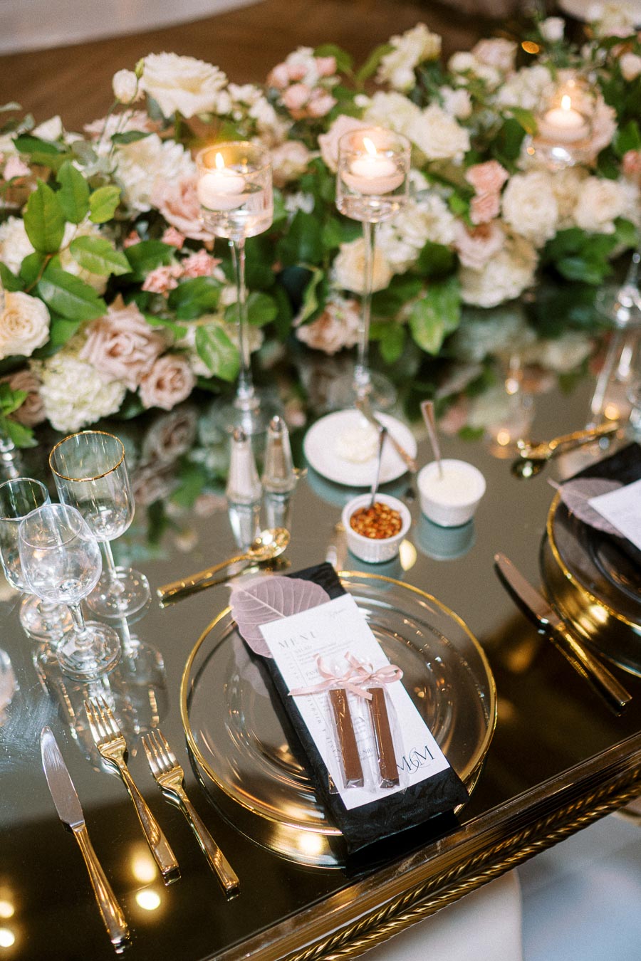 Elegant wedding table setting with mirrored surface, featuring gold-rimmed glassware, a floral centerpiece with white and