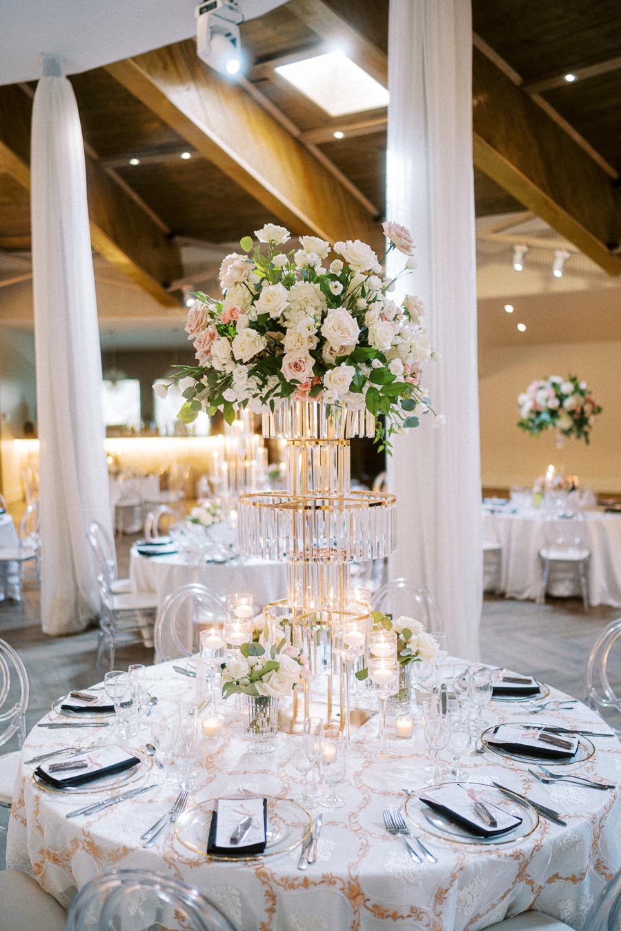 Elegant wedding reception table setup with a luxurious floral centerpiece featuring white and blush roses, surrounded by lit